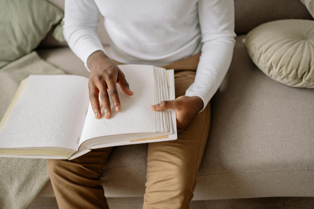 Visually impaired male, sat down and reading braille on sofa