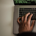 Hut Eight - Featured Image-New WordPress-Vulnerabilities-why maintenance matters-Article Banner - Hut Eight Close-up of hands typing on a silver laptop keyboard, with green code text visible on the screen.